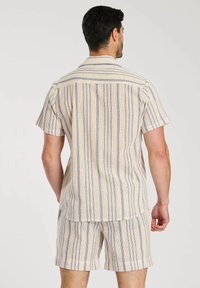 Set composto da una camicia a maniche corte e pantaloni corti in crema con strisce verticali blu. Il tessuto appare strutturato con leggere perforazioni e una vestibilità rilassata.