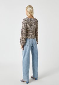 Langärmlige Bluse mit floralem Muster in Lila, Gelb und Grün, kombiniert mit hellblauen, weit geschnittenen Jeans und blauen Blockabsatzsandalen.