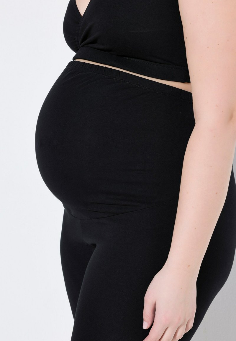 Czarna bluzka ciążowa i legginsy, wykonane z miękkiego materiału, dopasowany krój, z elastycznym pasem, podkreślające zaokrąglony kształt brzucha.