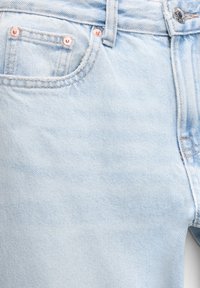 Vaqueros de denim azul claro con una textura suave, detalles en cobre en los bolsillos y los botones, y un diseño ajustado que presenta un estilo clásico de cinco bolsillos.