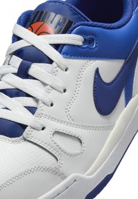 Sapatilha de couro branca com adornos azuis, língua em malha texturizada, detalhes perfurados e logótipo característico na lateral e na parte superior.