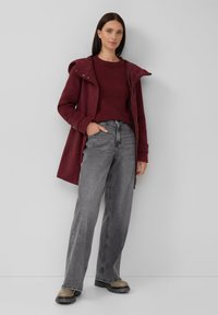Maronfarbener Mantel mit Kapuze, grauer Pullover, graue weit geschnittene Jeans und schwarze, strukturierte Stiefel. Elegantes Design mit lässiger Passform und funktionalen Taschen.