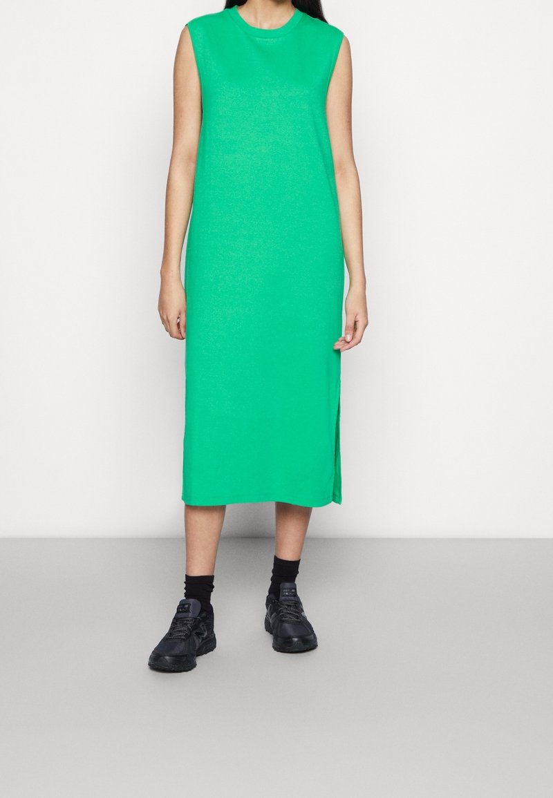 Robe midi verte sans manches avec fentes latérales, en tricot doux. Associée à des baskets noires et des chaussettes. Silhouette simple et droite.