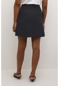 Dunkelblauer, glatter A-Linien-Rock mit hoher Taille und Saum über dem Knie. Kombiniert mit schwarzen Sandalen mit hohem Absatz.