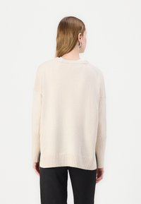 Suéter de malha bege claro com punhos e bainha canelados. Apresenta um corte descontraído e decote redondo, exibido por trás.