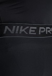 Svarta träningsleggings med en ribbad midja och "NIKE PRO" i reflekterande silverbokstäver. Slät textur med en figursydd design.