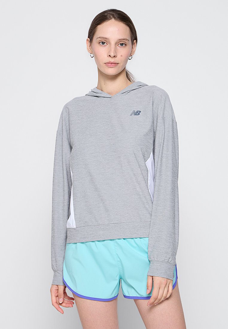 Sudadera con capucha gris de mangas largas, con un pequeño logotipo y paneles laterales blancos, combinada con pantalones cortos de color azul claro con acentos morados.