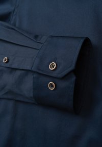 Navyblaues Hemd mit strukturiertem Design, zwei Messingknöpfen und einer glatten Textur mit schrägem Schnitt für eine taillierte Passform.