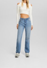 Top corto bianco a costine con spalline scoperte abbinato a jeans a gamba larga di colore blu chiaro. Sneakers con accenti grigi e bianchi completano l'outfit.
