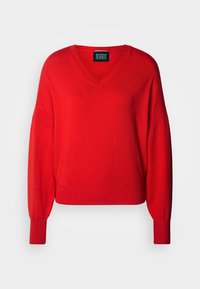 Pull rouge à manches longues avec col en V, poignets et ourlet côtelés, présenté à plat avec une étiquette de marque Scotch & Soda noire visible à l'intérieur du col.