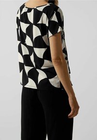 Haut à manches courtes noir et blanc arborant un motif géométrique avec des formes courbées. Tissu doux, coupe décontractée et décolleté en scoop.