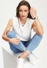 Top bianco senza maniche, jeans skinny strappati azzurri chiari e sneakers bianche; accessoriate con una collana e un orologio d'oro.