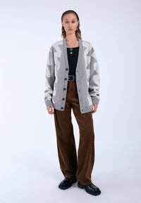 Grey cardigan with white zigzag pattern, button closure, and ribbed sleeves, paired with brown corduroy pants and black chunky shoes.
