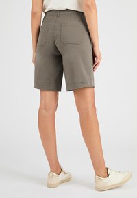 Pantaloni corti in cotone khaki con orlo arrotolato, tasche posteriori e vestibilità rilassata, abbinati a sneakers bianche con dettagli dorati.