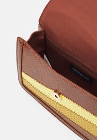 Bolso marrón con textura y un patrón de zigzag amarillo en la parte frontal. El interior cuenta con un forro de tela marrón y un bolsillo con cremallera.