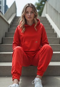 Felpa con cappuccio rosso e pantaloni jogging, realizzati in tessuto morbido, con tasca frontale, vestibilità comoda e dettagli in bianco sulle sneaker.