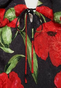 Tessuto nero con motivo floreale rosso e verde, dotato di chiusura a cravatta e finitura testurizzata. I dettagli includono un'apertura a cuore.