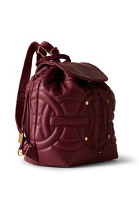 Dark red leather backpack with quilted circular patterns, gold-tone hardware, drawstring closure, and adjustable fabric shoulder straps.