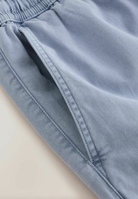 Pantalon avec ceinture élastique bleu clair, poche visible et coutures détaillées sur un tissu doux.