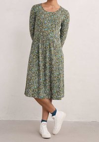 Zielona sukienka kwiatowa do kolan z długimi rękawami i okrągłym dekoltem. Posiada zwiewny fason i miękką, teksturowaną tkaninę. Połączona z białymi trampkami.