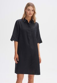 Abito camicia in lino nero con colletto, maniche corte e tasca sul petto. Tessuto leggero con una vestibilità rilassata, design minimale.