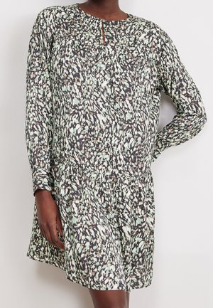 Robe à manches longues avec un motif abstrait noir, blanc et vert clair, avec une petite ouverture sur le devant et une taille froncée, portée par une personne.