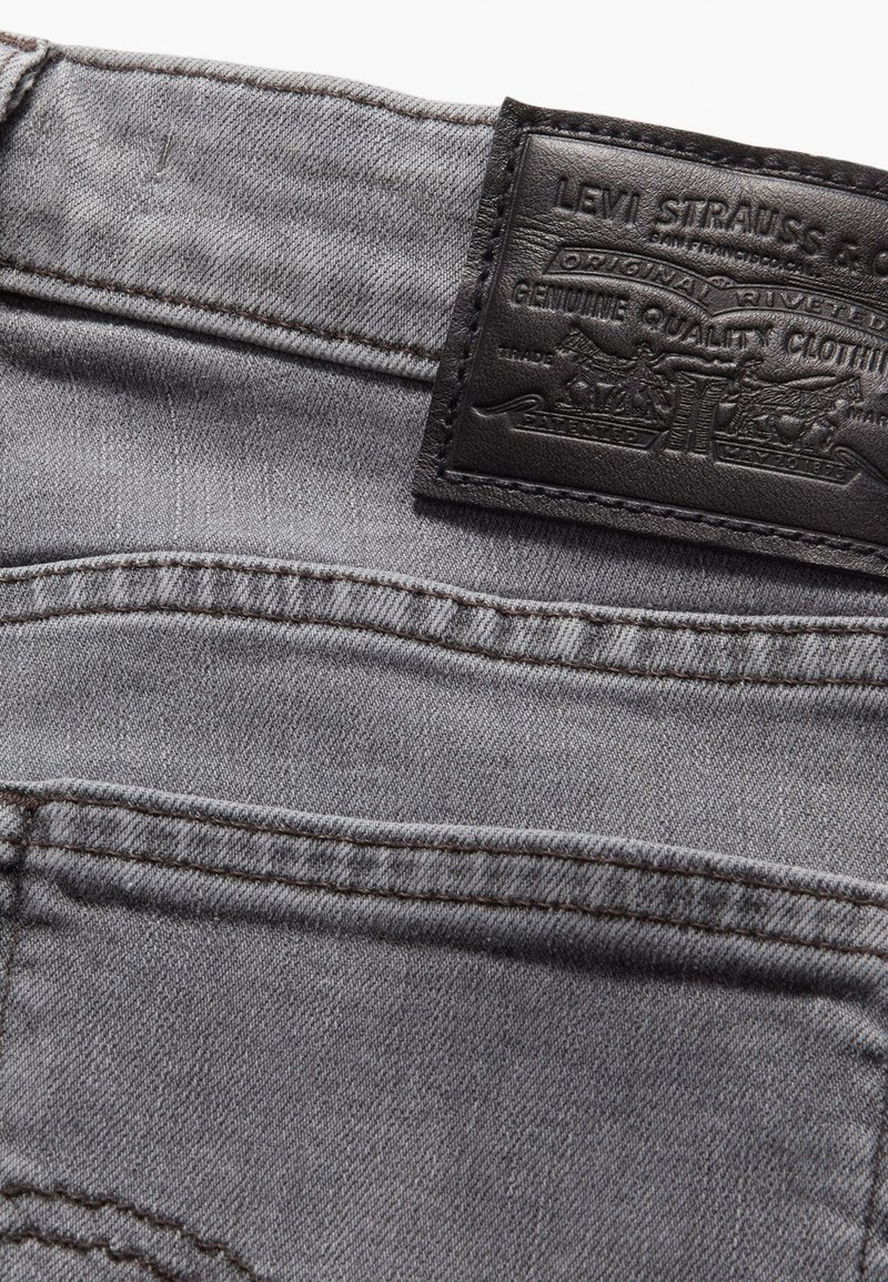 Grau denimstoff mit strukturiertem Oberflächen, versehen mit einem schwarzen Leder-Patch mit geprägten Markendetails und kontrastierenden Nähten.