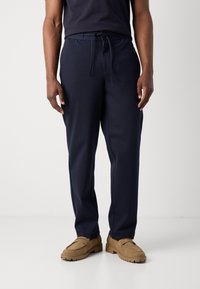Marineblå joggebukser laget av myk stoff, med elastisk midjebånd og snøring, sidelommer og rett snitt design.