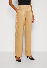 Beige satijnen wijde broek met een elastische tailleband en zijzakken, met een zachte textuur en een subtiele glans, gecombineerd met zwarte hakken.