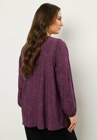 Blusa lunga viola a maniche lunghe con una stampa zebrina testurizzata, vestibilità leggermente ampia, maniche arricciate e orlo curvo.