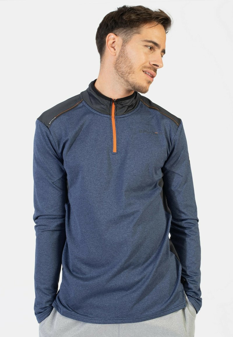 Camiseta deportiva de manga larga azul marino con un collar de media cremallera, hombros texturizados en negro y acentos naranjas. Tejido ligero, diseño que absorbe la humedad.