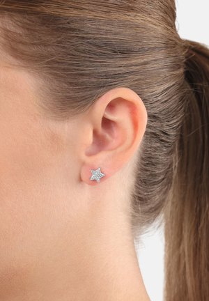 Orecchio di una donna con capelli castani raccolti, che indossa un orecchino a forma di stella in argento con piccoli pietre incastonate.