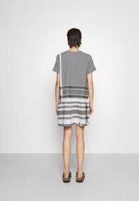 Sukienka z krótkim rękawem, charakteryzująca się mieszanką czarno-białych wzorów, w tym kropek i pasków, o luźnym kroju i długości do kolan.
