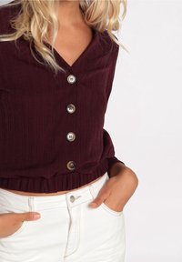 Top bordeaux à manches longues côtelé avec trois boutons et ourlet élastique, associé à un short en denim blanc avec une poche avant et un bouton argenté.