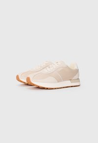 Beige fabric sneakers with tonal accents, textured panels, and a white sole. Features laces and a small logo on the side.