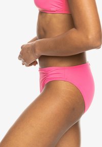 Roza bikini dno, izdelano iz gladkega, raztegljivega materiala. Ima nabran detajl na straneh, nizko pasovo obliko in enobarvni dizajn.