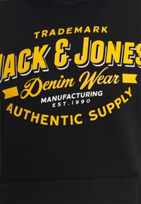 Felpa nera con testo audace giallo e bianco con il nome del marchio "Jack & Jones", un logo curvo e la data di fondazione.