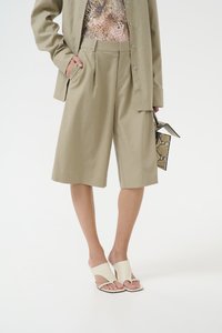 Shorts beige ajustés avec des plis, associés à un haut à motifs et des sandales blanches à enfiler. Les accessoires comprennent un petit sac texturé.