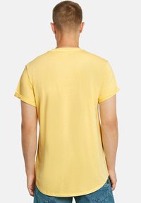 T-shirt giallo a maniche corte realizzato in tessuto morbido, con bordo arrotondato e maniche arrotolate. Il retro presenta una superficie liscia e una vestibilità casual.