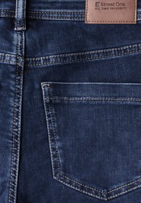 Dunkelblå denimjeans med bakficka, med kontrasterande sömmar och en brun etikett med texten "Street One" vid midjan.