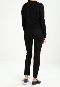 Pull en maille noire et jean skinny noir. Texture lisse, coupe ajustée et ourlet légèrement raccourci. Chaussures bleues avec semelles blanches.