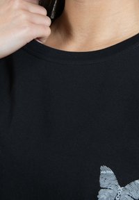 Sort t-shirt med rund halsudskæring, der har et lyseblåt grafisk design på nederste venstre side, lavet af blødt bomuldsstof.