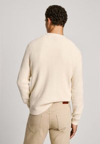 Kremno obarvana rebrasta pulover s okroglim ovratnikom, dolgimi rokavi in sproščeno prileganje, v kombinaciji s svetlobeznimi hlačami z dodatnim žepom.