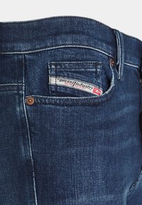 Jeans de mezclilla azul oscuro con un diseño clásico, costuras visibles y un bolsillo trasero con una etiqueta de "Diesel Industry".