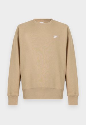 Halványbarna Nike pulcsi, kerek nyakkivágással, hosszú ujjal és fehér logóval a mellkason. Az anyaga lágy, sima textúrájú.