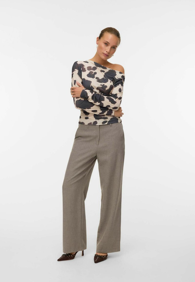 Langsleeve top met een beige en donkerbruin dierenprint en een off-the-shoulder ontwerp. Gecombineerd met grijze wijde pantalons en bruine hakken.