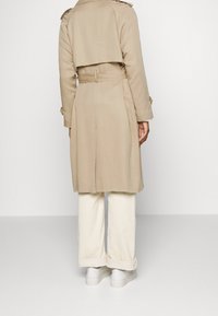 Beige trenchcoat with a belted waist, shoulder epaulettes, and a split back, combined with white wide-leg trousers and white sneakers.