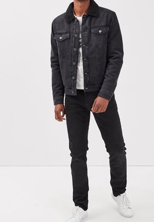 Veste en denim noire avec col en shearling, dotée de deux poches poitrine, fermeture à boutons, et coupe ajustée, associée à un jean slim noir et des baskets blanches.