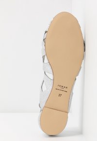Semelle d'une sandale à lanières argentées montrant une semelle lisse couleur beige avec la taille 37 et l'inscription "JONAK PARIS MADE IN PORTUGAL".