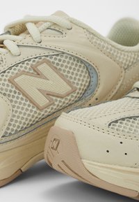 Baskets beige avec tige en mesh, semelle en caoutchouc et logo N texturé. Comprend des lacets crème et des accents gris clair sur le côté.